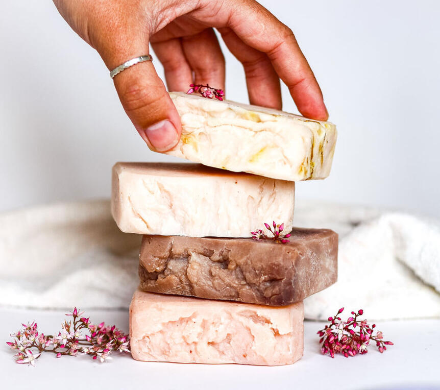 stack of handmade soaps being picked up by a hand with a cozy background